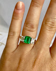 Close-up of green emerald cut center stone flanked by white diamonds – Cherry Pick Diamonds