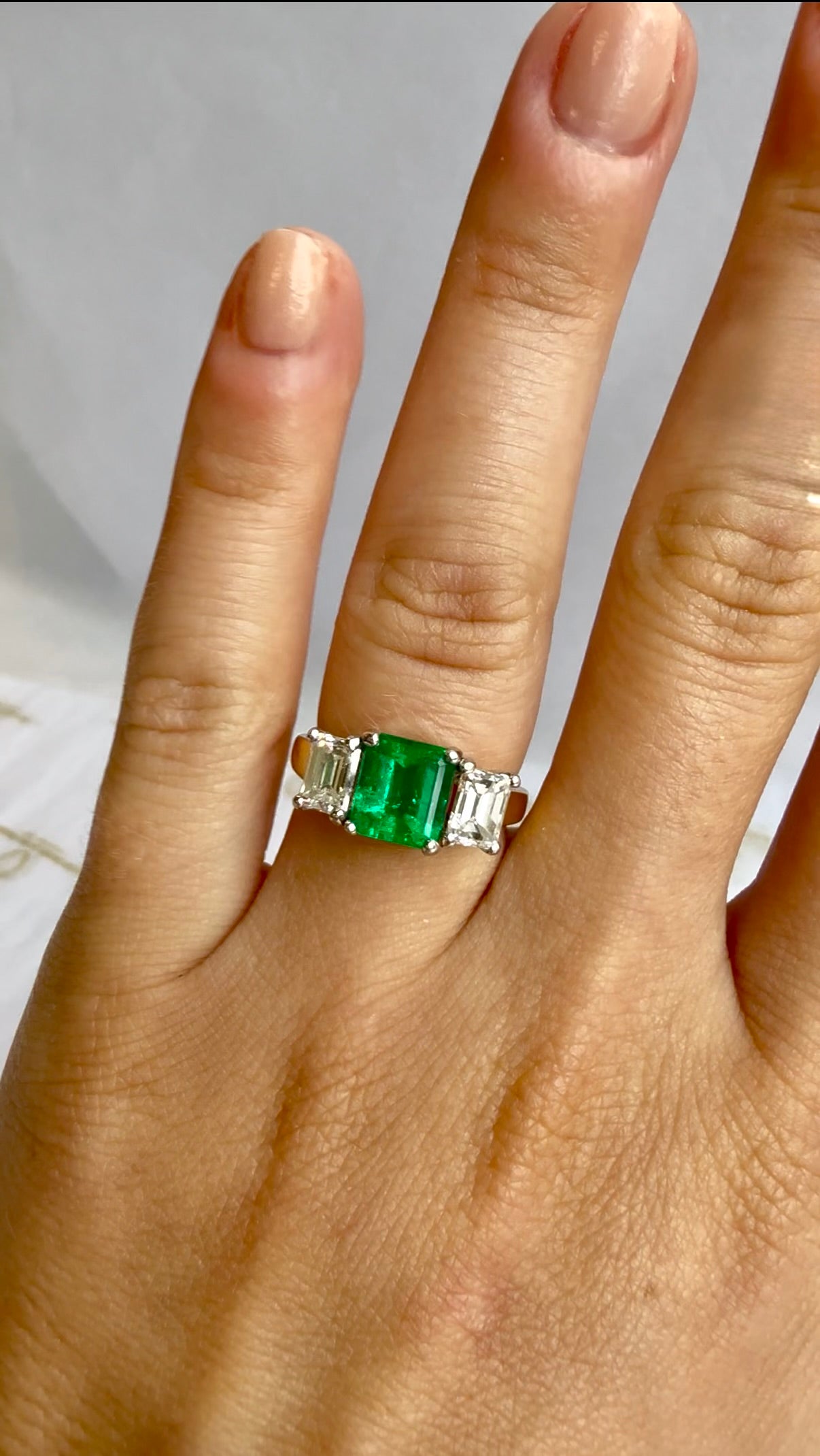 Close-up of green emerald cut center stone flanked by white diamonds – Cherry Pick Diamonds