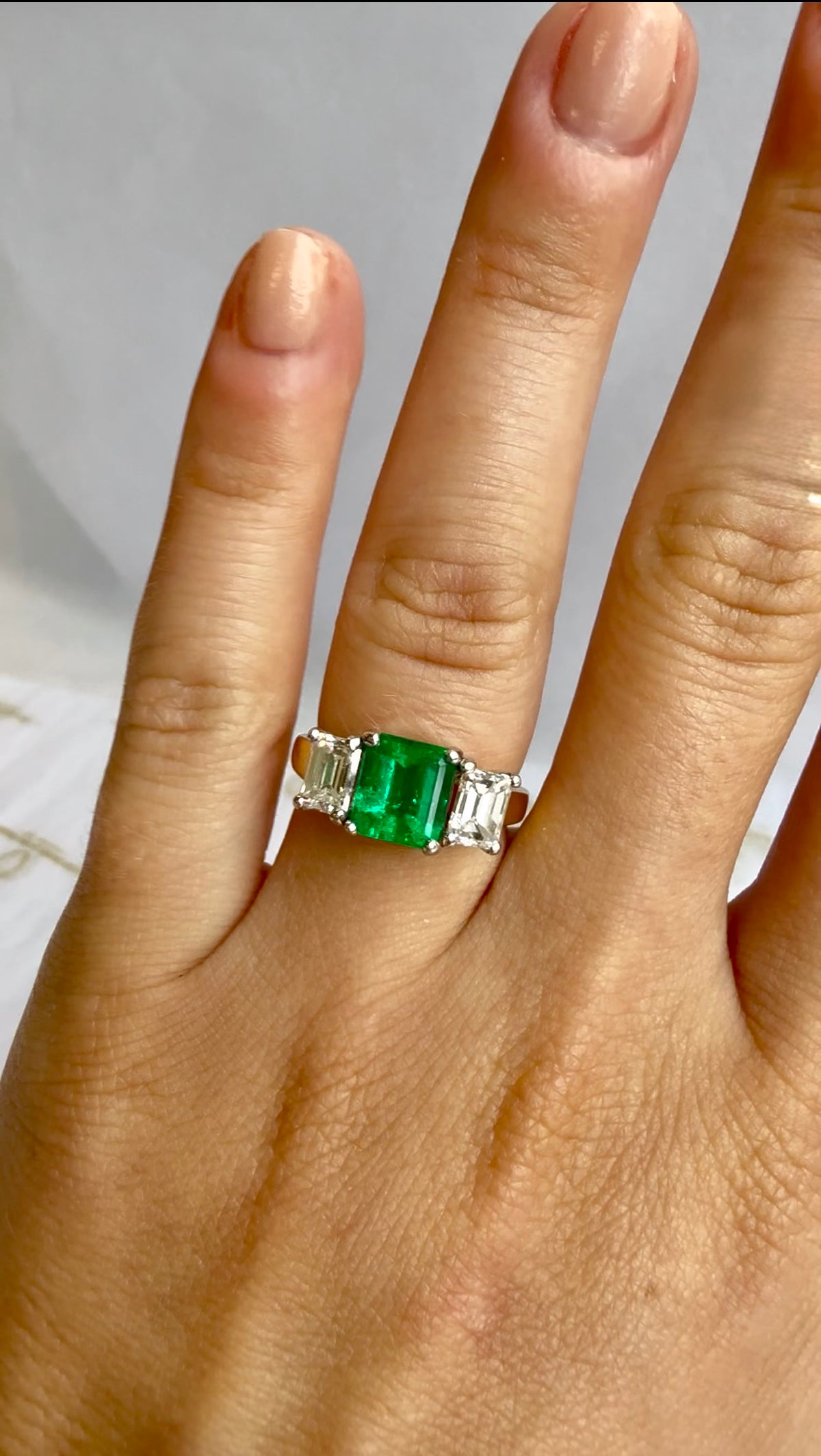 Close-up of green emerald cut center stone flanked by white diamonds – Cherry Pick Diamonds